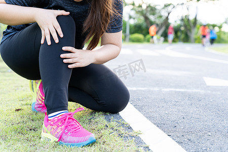受伤女孩摄影照片_亚洲女性在公园的路上跑步时用手抓住膝盖受伤，锻炼概念造成的伤害。