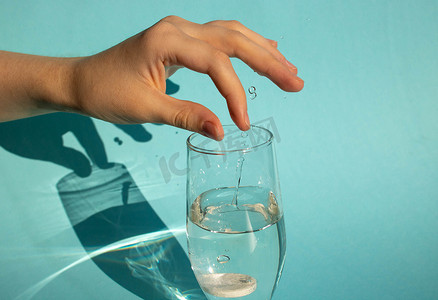 在蓝色背景下，一只手将溶解的起泡阿司匹林片剂滴入一杯水中