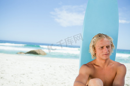 泳衣帅哥摄影照片_金发男子坐在他的冲浪板前，一边看着一边