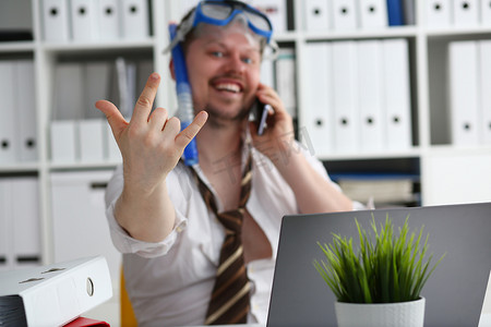 戴着游泳镜的旅游公司情绪开朗的男经理正在工作场所用手机聊天