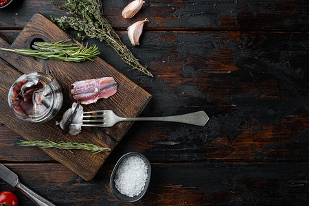 盐渍凤尾鱼片，在木制切菜板上，在旧的深色木桌背景上。