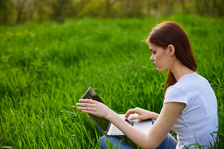 年轻漂亮的女人在草地上使用笔记本电脑