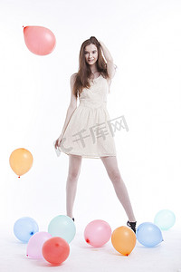 白色背景下，穿着裙子、地板上放着气球的漂亮年轻女子