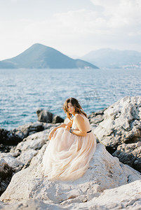 新娘坐在海边的岩石上，背靠群山