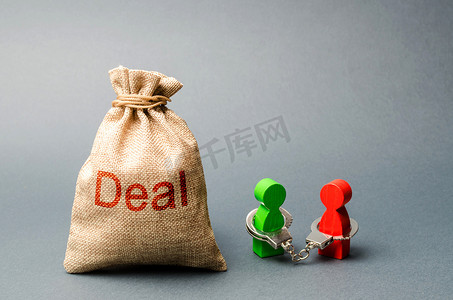 两个人被铐在一起，站在标有 Deal 标签的袋子旁边。
