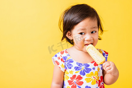 吃东西的小孩摄影照片_婴儿或小孩，可爱的小女孩，迷人的笑，微笑，穿着鸡巴图案的衬衫，拿着甜甜的木制冰淇淋