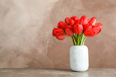 棕色背景下桌上有美丽红色郁金香的花瓶，文字空间