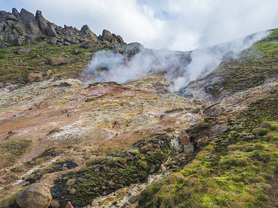 气孔摄影照片_Reykjadalur 山谷的彩色流纹岩红色、橙色和黄色喷气孔，有锋利的岩石、草地和地热蒸汽。 