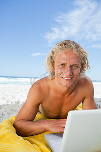微笑的金发男人一边用笔记本电脑一边看着相机