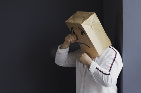 悲伤的男人头上顶着一个袋子，画着哭泣的表情符号。
