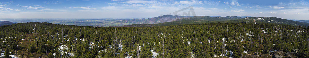 Jizera Mountains jizerske hory 的广阔全景景观，从 holubnik 山的山顶可以看到郁郁葱葱的绿色云杉林、树木、山丘和田野，春天还有积雪，蓝天背景