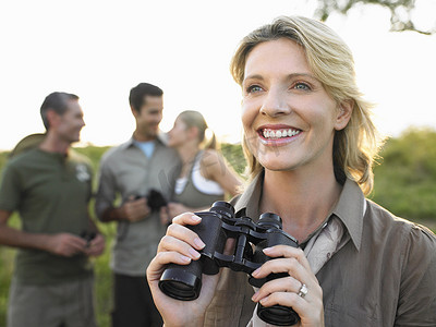 中筒摄影照片_微笑的女人手持双筒望远镜，背景中朋友模糊