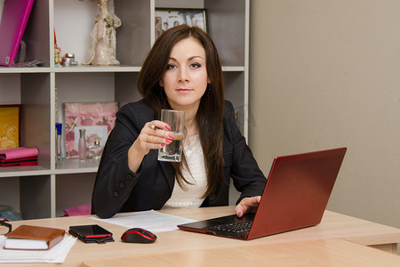 电脑前的女商人拿着一杯水