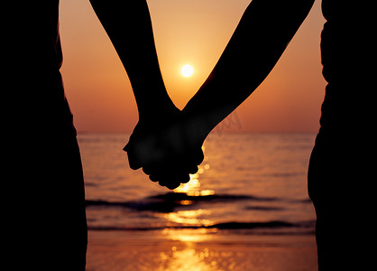 夕阳下手牵手的情侣剪影。