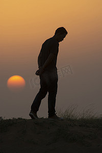 流浪的人摄影照片_黄昏时分走在沙漠沙丘上的人，风景照片