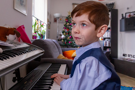 客厅钢琴摄影照片_男孩在圣诞节弹钢琴