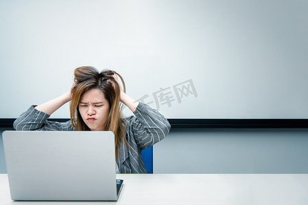 女性生气摄影照片_在办公室用笔记本电脑工作的女人很生气