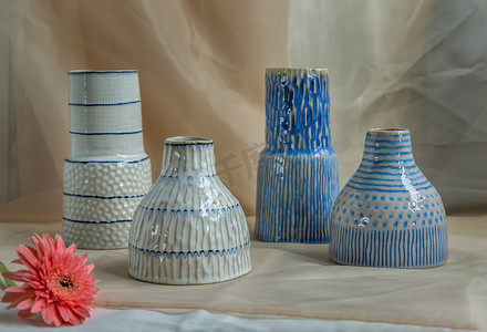 四个蓝色和白色手工陶瓷花瓶，粉色花朵装饰在腮红纹理桌布上。