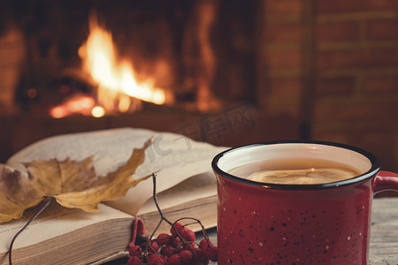 红杯配热茶，壁炉前放着一本打开的书，壁炉概念的舒适、放松和温暖