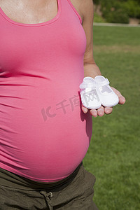 粉红色孕妇摄影照片_手拿短靴的粉红色孕妇