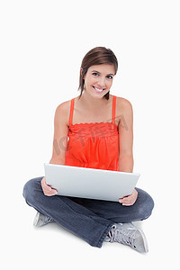 美丽的少女盘腿坐着，腿上放着一台笔记本电脑