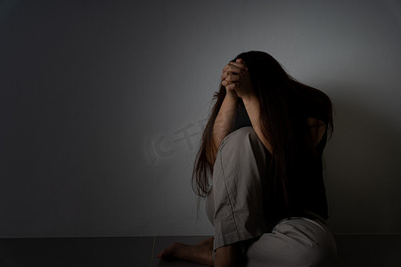 暴风哭泣摄影照片_悲伤的女人抱着她的膝盖，独自坐在黑暗的房间里哭泣。