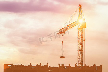 一队建筑工人的剪影和一台起重机在落日的天空背景下建造建筑物。
