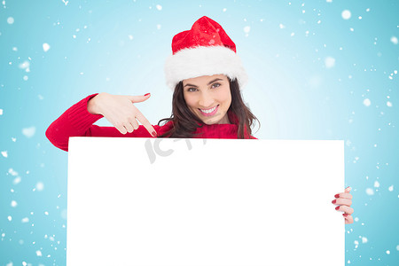 戴着圣诞帽的漂亮黑发女郎指向白色海报的合成图像