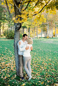 男人拥抱站在黄叶梧桐树下的女人