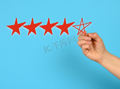 客户评分摄影照片_打出五颗红星，一只女手在蓝色背景上画画，评分很高