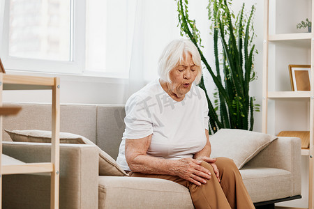 老年妇女坐在沙发上腿部剧痛，老年健康问题，生活质量差。