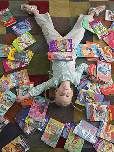 书籍角度摄影照片_女孩躺在图书馆地板上的高角度视图，周围散落着书籍