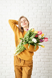 美女拿着花摄影照片_穿着黄色衣服的快乐美女拿着一束郁金香