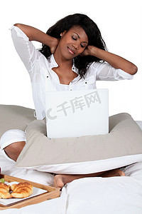 黑人妇女盘腿躺在床上，带着笔记本电脑