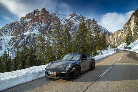 意大利，多洛米蒂山，卡纳泽伊，2019 年 5 月 1 日：昂贵的跑车在白雪覆盖的山脉白云岩的扭曲道路上停下来，保时捷 911 Turbo 4 GTS，联合国教科文组织纪念碑，晴朗的天气