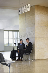 两名商人在机场大厅使用笔记本电脑