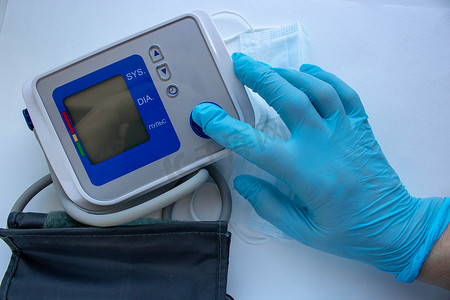 男性手戴手套，在白色背景上隔离的血压计上按下开始按钮。