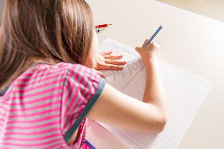 孩子用蓝色铅笔蜡笔在书桌上写作业