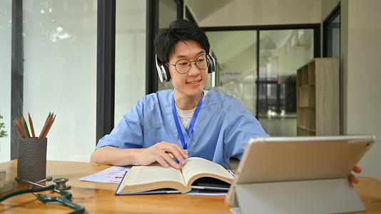 在图书馆里戴着耳机和使用数字平板电脑的年轻男医学生。