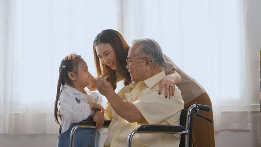 坐在轮椅上的残疾老人与女儿和孙女在客厅里微笑着一起玩耍