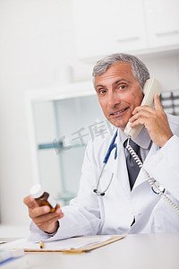 医生拿着药摄影照片_医生坐着拿着药盒和电话