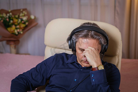 听音乐摄影照片_50 岁的男人坐在椅子上，在家里用耳机听音乐。