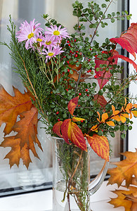 花朵和叶子摄影照片_窗台上有一束秋天的花朵和叶子。