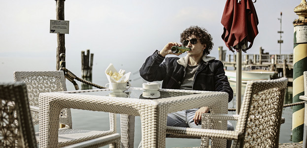 忧郁摄影照片_忧郁的年轻人在码头的吧台上喝啤酒