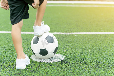脚踩足球摄影照片_一个穿着白色运动鞋的男孩脚踩着足球。