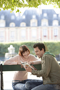 快乐的年轻夫妇在城市公园长椅上阅读指南