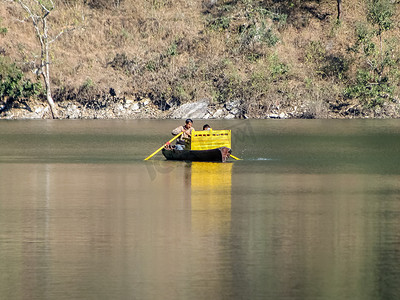 船夫和游客在 Bhimtal 湖水域划着他的黄色小船。