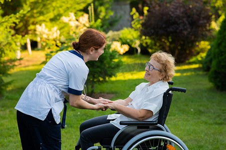 一名护士用手扶着一位坐在轮椅上的白人老年妇女作为支撑。