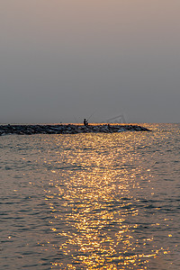 早上在平静的海滩上拿着钓鱼竿的钓鱼者。
