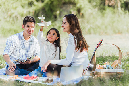 快乐的太阳摄影照片_快乐的家庭玩得开心，享受户外坐在野餐毯上玩玩具飞机